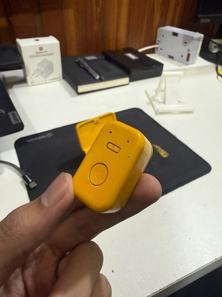 The same wearable coaching device held in hand, single-button enclosure